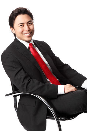 Young serious businessman sitting down in a chair wearing a suit and red tie  White background の写真素材