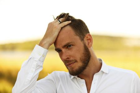 An attractive man in his 20s wearing a white shirt standing outside on a sunny summer day, with a big yellow field behind him.の写真素材
