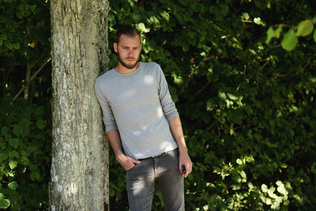 An attractive man wearing jeans,boots and a shirt standing with a green background on a sunny summer day.の写真素材