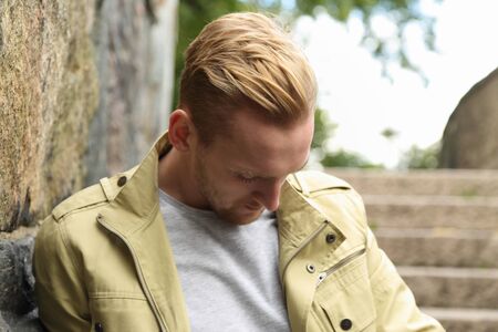 An attractive man standing, leaning against a stone wall wearing a yellow jacket outside on a sunny day.の写真素材