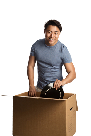 A man in his 20s wearing a blue shirt and pants, packing and carrying a cardboard box. White background.の写真素材
