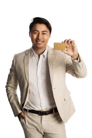 Attractive man in a bright beige suit, holding a golden VIP card smiling towards camera. White background.の写真素材