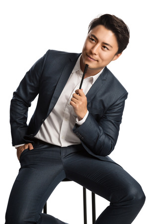 Creative businessman in a blue suit and white shirt, holding a pen thinking. White background.の写真素材