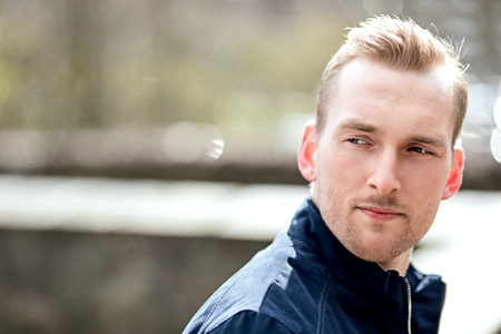 Handsome blonde man wearing a blue jacket and white tshirt leaning against a wall outdoors on a sunny day, trendy and fashionable.の写真素材