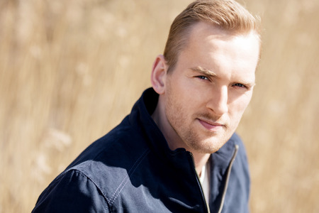 Portrait of a focused man standing outside with a wheat field behind him on a sunny spring day,の写真素材