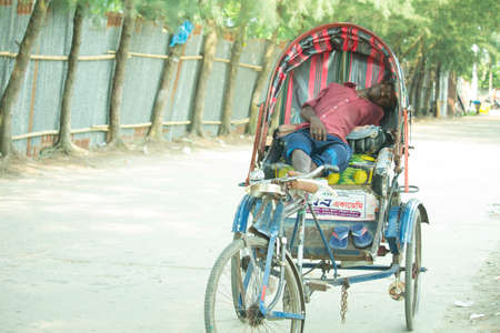 Jun 12, 2019, Barisal, Bangladesh. A rickshaw puller is tired of driving a rickshaw.  Resting on top...