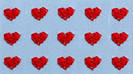 A close-up, top-down view of a blue fabric background with a repeating pattern of small, red embroidered hearts. The hearts are stitched with visible thread, creating a textured effect. The arrangement is neat and symmetrical, with three rows of five hearts each.の素材