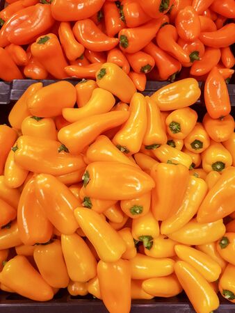 a pile of yellow and orange Mini peppers on sale in a shop