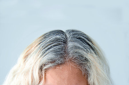 head woman with gray root showing blonde hair light backgroundの写真素材