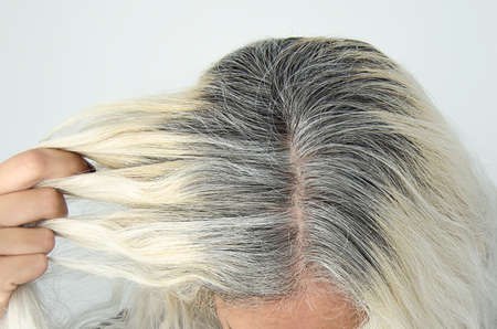 head woman with gray root showing blonde hair light backgroundの写真素材
