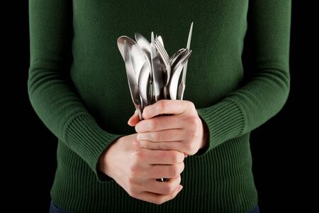 woman in a green jumper holds a bunch of silverware in her handの写真素材
