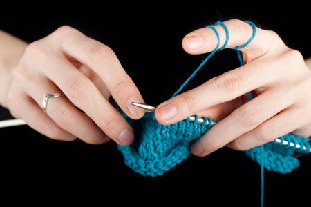 Hands of a young woman knitting with blue wool