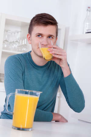 young man drinking a glass of orange juice in his kitchenの写真素材