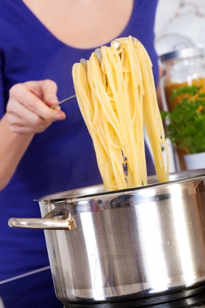 female hands raising cooked spaghettis out of the potの写真素材