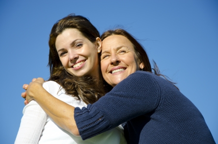 Beautiful mother and daughter hugging each other on a sunny  day outside, with clear blue sky as background and copy space の写真素材