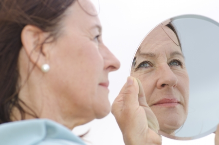 Portrait of an attractive middle aged woman looking into a mirror, with focus set on the mirror image の写真素材
