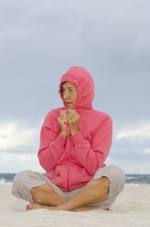 Portrait happy mature woman keeping herself warm at a stormy day at the beach, isolated with ocean and dark clouds as background and copy space の写真素材
