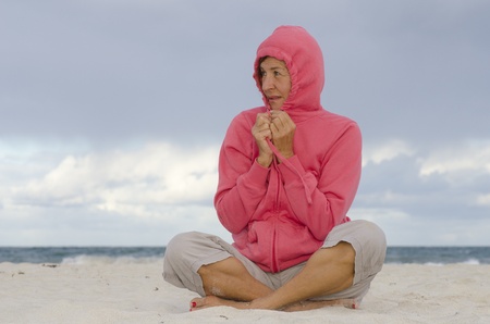 Portrait happy mature woman keeping herself warm at a stormy day at the beach, isolated with ocean and dark clouds as background and copy space の写真素材