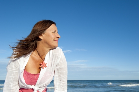Relaxed and attractive looking senior woman enjoying sunshine at beach, isolated with ocean and sky as background and copy space.の写真素材