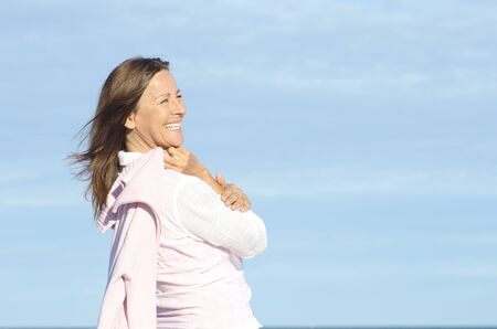 Cheerful, happy smiling attractive senior woman enjoying retirement, isolated, with blue sky as background and copy space.の写真素材