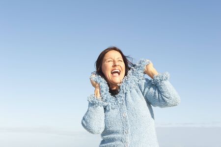 Portrait of beautiful and cheerful mature woman with warm jumper, enjoying winter sun, isolated with blue sky as background and copy space.の写真素材