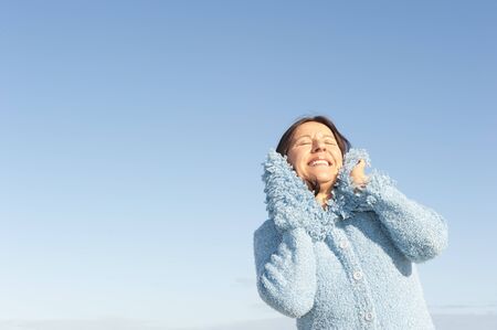 Portrait of beautiful and happy mature woman with warm jumper, enjoying winter sun, isolated with...
