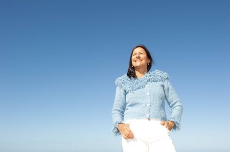 Portrait of confident and happy relaxed looking attractive senior woman enjoying active retirement in winter sun, isolated with blue sky as background and copy space の写真素材