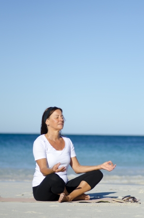 Attractive and active senior woman keeping fit with yoga and meditation at beach, isolated with ocean and blue sky as background and copy space.の写真素材
