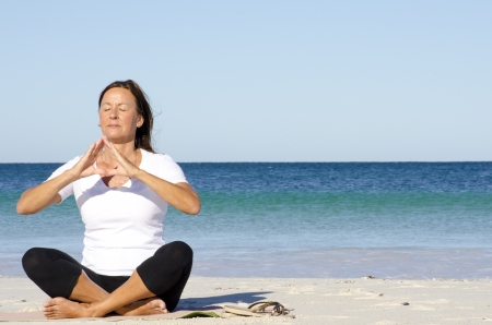 Attractive and active senior woman keeping fit with yoga and meditation at beach, isolated with ocean and blue sky as background and copy space.の写真素材