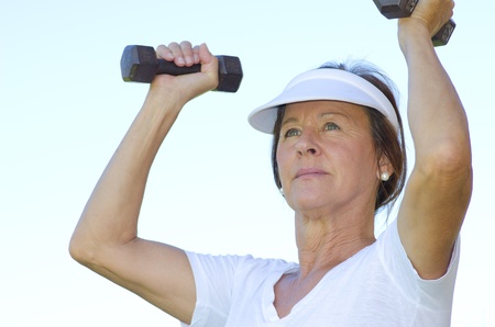 Portrait attractive fit and active senior woman exercising with weights, isolated with blurred outdoor background.の写真素材