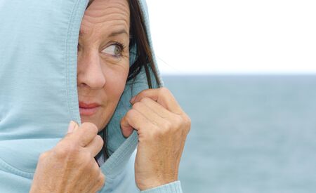 Portrait of a pretty looking mature woman in her fifties wearing a hooded jumper covering her head,...