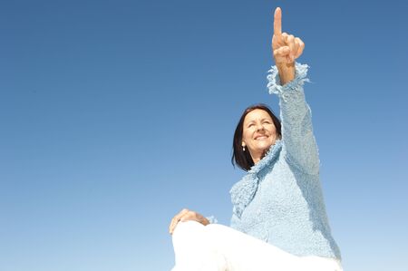 Happy confident and focused mature woman pointing with finger, isolated with blue sky as background and copy space.の写真素材
