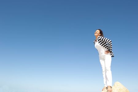 Confident, happy, successful and attractive mature, senior woman on top of rock, mountain, isolated with blue sky as background and copy space.の写真素材