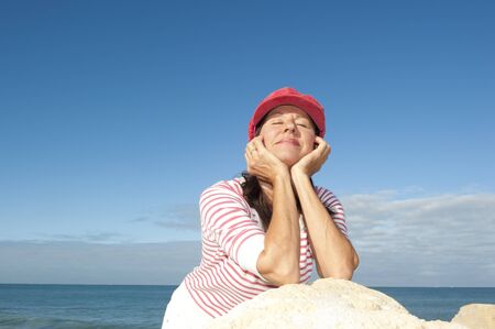 Portrait of relaxed and attractive looking senior woman enjoying active retirement and leisure time at sea, isolated with ocean and blue sky as background and copy space の写真素材