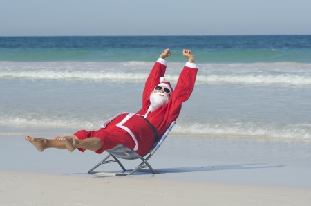 Santa Claus happy relaxed sitting with hands up at beachの写真素材