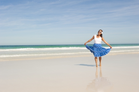 Happy mature woman wearing white top and blue skirt at tropical beach, isolated with ocean and blue sky as background and copy space の写真素材