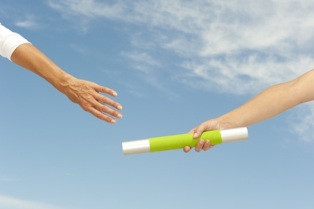 Hands of track and field athletes with relay baton, symbol for teamwork, partnership, cooperation, isolated with blue sky as background and copy space.の写真素材