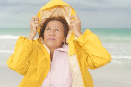 Portrait attractive and worried mature woman with yellow  protective raincoat, isolated with ocean...