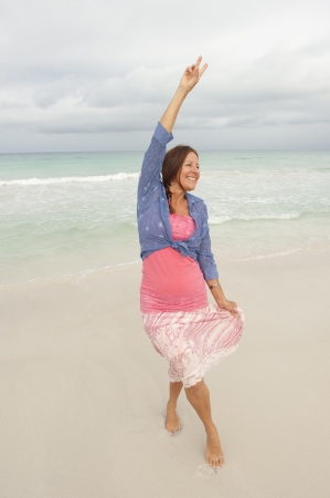 Sexy middle aged woman with arms up happy and confident at beach vacation enjoying active retirement, isolated with ocean and cloudy sky as background and copy space.の写真素材