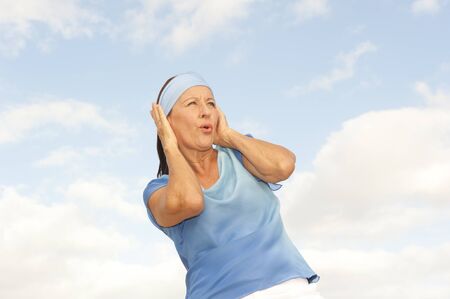 Portrait attractive looking mature woman with surprised and stressed facial expression outdoor, isolated with cloudy blue sky as background and copy space.の写真素材