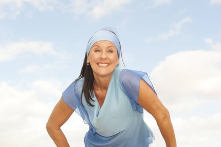 Portrait relaxed confident attractive mature woman outdoor wearing blue headband and blouse, isolated with cloudy blue sky as background and copy space.の写真素材