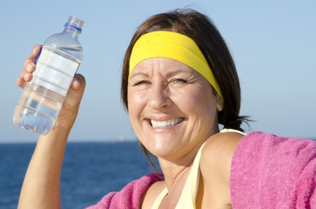 Portrait attractive fit and healthy, sporty and exercising, active retired mature woman drinking water out of bottle outdoor, isolated with ocean and blue sky as blurred background.の写真素材