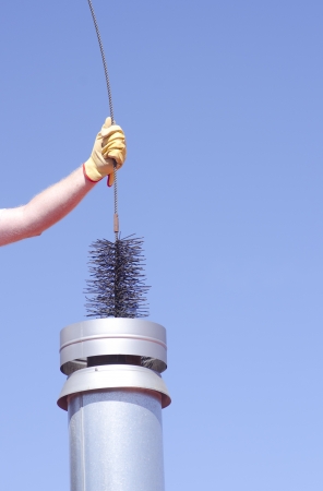Arm with yellow glove holding sweeper to clean chimney on house, isolated with blue sky as background and copy space.の写真素材