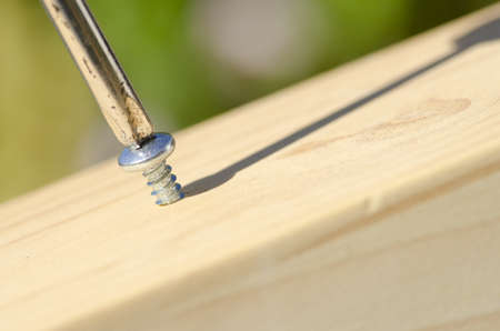 Detailed closeup of screwdriver and screw in timber panel outdoor with shadow and blurred background and copy space.の写真素材