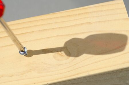 Detailed closeup of screwdriver and screw in timber panel outdoor with shadow and blurred background and copy space.の写真素材