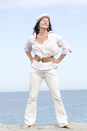 Portrait attractive middle aged woman standing happy and relaxed smiling in confident pose at coastの写真素材