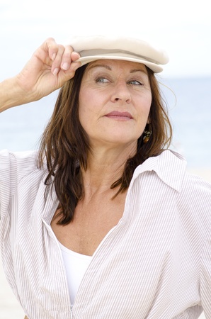 Portrait happy confident attractive mature woman wearing a cap, isolated outdoor with white bright blurred background.の写真素材