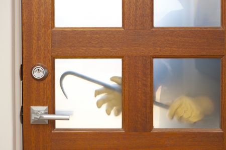 Hands of Burglar, thief  with gloves, holding crowbar trying to break in home, unlock door, blurred visible silhouette behind milky windows, with copy space.の写真素材