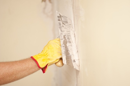 Closeup of palette-knife or scraper and cement filling for house renovation construction in hands of handyman and worker fixing interior wall, with blurred background and copy space.の写真素材