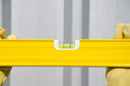 Hand of construction worker with glove on spirit or water level tool outdoor, with silver metal wall as background and copy space.の写真素材